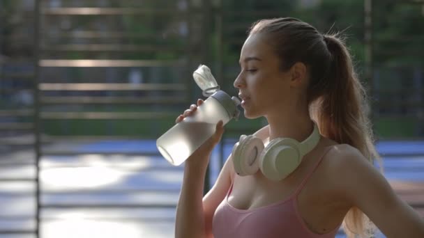 Sidovy Yoga Kvinna Dricksvatten Från Sport Flaskan Bär Hörlurarna Halsen — Stockvideo