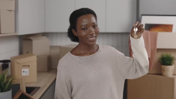 非洲裔美国妇女拿着房子钥匙 看着相机 在新家的室内微笑 画像的女主人站着 拿着钥匙 新家和搬家的概念 — 图库视频影像