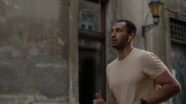 Eski kasaba sokaklarında kulaklık takıp müzik dinleyen Afro-Amerikan bir adamın yan görüntüsü. Spor ve sağlıklı yaşam tarzı kavramı