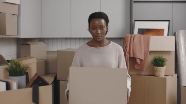 手に大きな箱を持っているアフリカ系アメリカ人女性の笑顔の肖像画は カメラに示す 女性の入力は 新しいアパートに移動することに満足 新しい家 移転の概念 — ストック動画