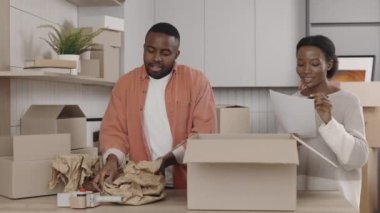 Afro-Amerikalı çift tabakları kutulara koyuyor ve kadın da listeyi hazırlıyor. Yeni ev ve taşınma kavramı
