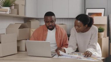 Afrikalı Amerikalı çift gelecekteki iç mekanlar için tasarım seçiyor. Mutlu çift, ev tasarımcısının dizüstü bilgisayardaki uygun renkleri kontrol ettiğini söylüyor. Yeni ev ve taşınma konsepti