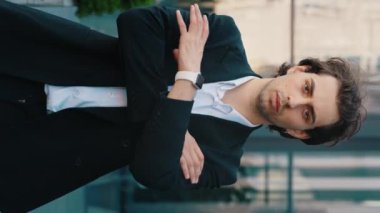 Dikey video. Beyaz iş adamının resmi süitteki portresi iş merkezinin yanında duruyor, ellerini çaprazlayarak kameraya bakıyor. Erkek patron iş yerinin yakınında kameraya bakıyor.
