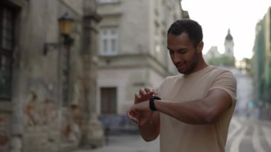 Aktif bir Afrikalı Amerikalı 'nın spor yapmadan önce spor yaparken takip cihazını kullanmasının portresi. Eski kasaba sokaklarında duruyor. Spor ve sağlıklı yaşam tarzı kavramı