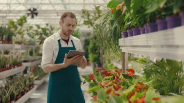 Sera çiçeklerinde dikilen beyaz erkek işçi dijital tablete bilgi yazıyor. Çiçekçide bilgisayarla çalışan genç bir çalışan. Çiçekçi kavramı