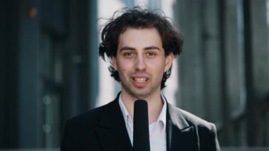 Açık hava haberleri için mikrofonla konuşan beyaz, yakışıklı bir erkek gazetecinin portresi. Takım elbiseli ve mikrofonlu bir muhabir. Kapat.