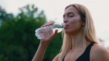 Parkta duran, plastik şişeden su içen Kafkasyalı koşucunun yakın görüntüsü. Koşudan sonra dinlenen bayan sporcu. İnsanlar ve spor konsepti