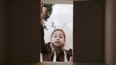 Beyaz kadın çocuk, içinde noel hediyesi olan karton kutuyu açıyor ve olumsuz bir yüz ifadesiyle içine bakıyor. Beklentilerden dolayı hayal kırıklığı ve hayal kırıklığı..