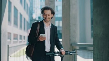 İş adamı iş merkezine gidiyor, elinde elektrikli bisikletle sosyal medyadaki iş sohbetlerine cevap veriyor. Erkek patron iş yerinin yakınında akıllı telefon kullanıyor, mesajlaşıyor.