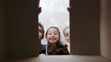 Parti şapkalı şirin kızı olan beyaz bir aile, doğum günü hediyesiyle karton kutuyu açıyor. Negatif duygular ve şaşkınlık..