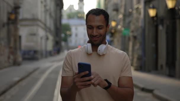Afrikanischer Mann Mit Kabellosen Kopfhörern Der Mit Seinem Neuen Smartphone — Stockvideo