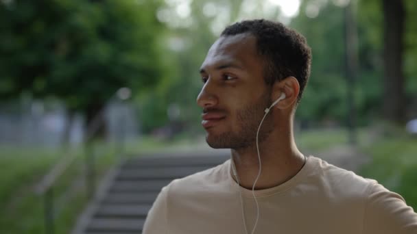 Портрет Африканского Американца Наушниках Слушающего Музыку Смотрящего Камеру Фоне Парка — стоковое видео