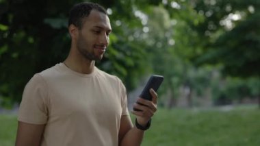 Park arka planında telefonuna mesaj atan Afro-Amerikan sporcunun portresi. Erkek koşucu eğitimden sonra yeni akıllı telefon uygulaması kullanıyor. Spor ve sağlıklı yaşam tarzı kavramı