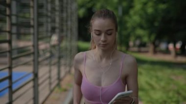 Genç bayan koşucu elinde telefonla koşmaya başlar ve kulaklıkla dinlemek için müziği açar. Dışarı çıkın. Spor ve sağlıklı yaşam tarzı kavramı