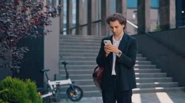 Kafkasyalı işadamı iş merkezinin yanında duruyor ve sosyal medyadaki iş sohbetlerine cevap veriyor. Erkek patron akıllı telefon kullanır, müşterilerle mesajlaşır, uygulamaları yürütür.