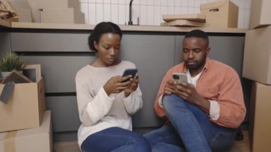 Afrika kökenli Amerikalı bir çift yeni ev arka planında telefonlarını kaydırıyor. Yeni ev ve taşınma konsepti