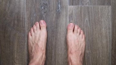 Bare feet of adult man is stepping on laminate floor in home, moving fingers and whirling, closeup view. High quality FullHD footage