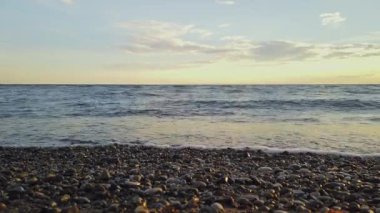 Şeffaf deniz dalgaları kıyıya yuvarlanıyor. Dalgaya ve ön planda çözünmüş deniz çakıllarına odaklan. Yüksek kalite 4k görüntü