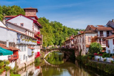 Kırmızı balkonları ve çiçekleri sakin bir nehirden geçen Fransız beyaz kasabasının panoramik manzarası. Saint-Jean-Pied-de-Port, Fransa