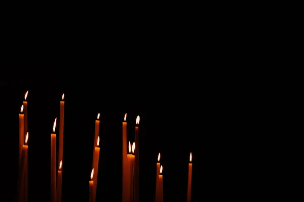 Thin wax candles burning over black background