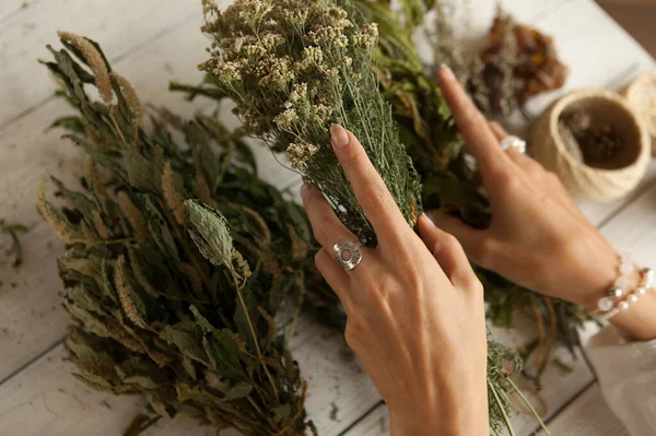 bunch of dried medicinal herbs in women\'s hands,  collection of medicinal herbs, white wooden table