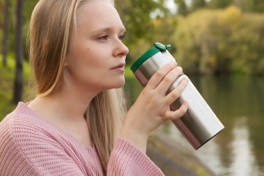 Genç bir kız termostan içer, sıcak bir içecekle termostan içer, sarışın bir kız yürüyüşe çıkar.
