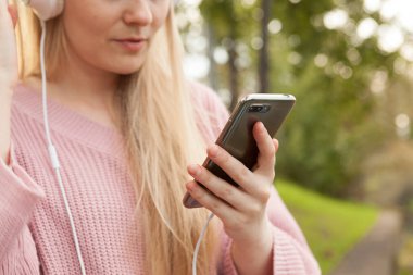  Beyaz kulaklıklı genç bir kız müzik dinliyor, elinde akıllı bir telefonla kulaklıkla yürüyen, müzik dinleyen bir kız.