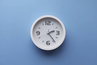 White wall clock on the wall. Minimalist flat lay image of plastic wall clock over blue turquiose background with copy space and central composition.