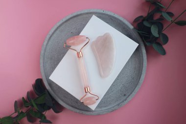 Yüz masajı seti. Yüz silindiri ve gua sha masaj aleti, doğal pembe taşlardan yapılmış, refah, yüz fitness konsepti, şık tek renkli kart, lüks afiş.
