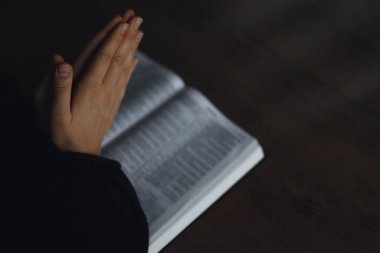 İncil'in üzerine eller kadın. o okuma ve İncil'de karanlık bir alan üzerinde ahşap masa üzerinde dua.