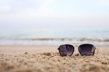 Beautiful background of Turquoise Sea with sunglasses lying on the sand beach. The concept of Rest Vacation. Wide Horizontal Colorful Wallpaper with selective focus and copy space.