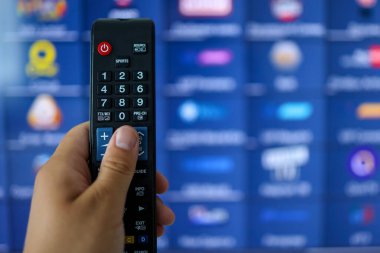 Smart tv and hand pressing remote control. Hand holding TV remote control with a television in the background. Close up.