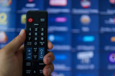 Smart tv and hand pressing remote control. Hand holding TV remote control with a television in the background. Close up.