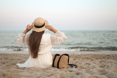 Portre geri görüntülemek beyaz elbise ve şapka mavi okyanus ve gökyüzü, izole deniz arka plan doğru bakan oturan kadın