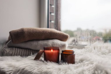 Warm and cozy autumn concept of candles and sweaters on the windowsill.