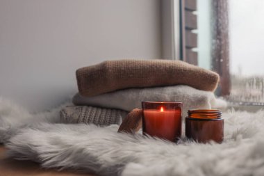 Warm and cozy autumn concept of candles and sweaters on the windowsill.