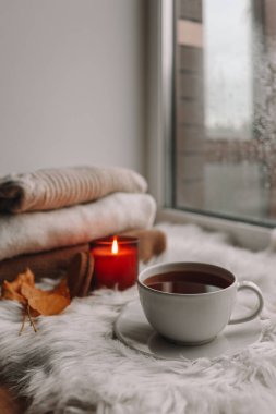 A cup of tea and a burning candle on the windowsill. Cozy autumn photo.