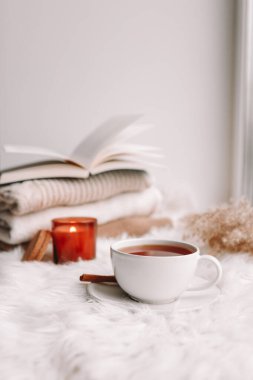 A cup of tea on the window with burning candles and sweaters.