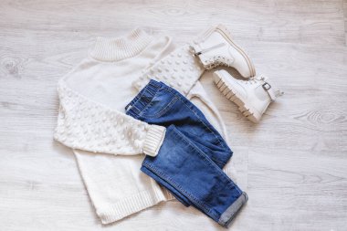 Womens autumn flat clothes with warm white sweater, blue jeans and white shoes, feminine fashionable outfit on white sheet, copy space