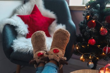 Feet in cute slippers on the background of the Christmas tree.