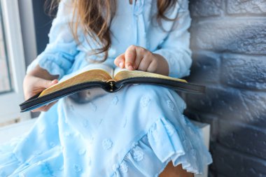 Little girl hands folded in prayer on a Holy Bible in church for faith concept in vintage color tone.