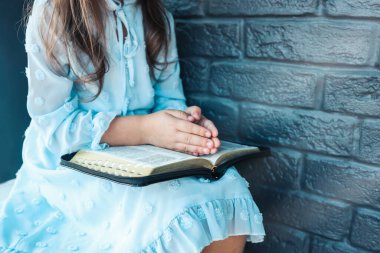 Little girl hands folded in prayer on a Holy Bible in church for faith concept in vintage color tone.