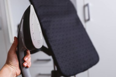 Woman using steaming iron to ironing fashion shirt in laundry room. Girl doing stream vapor iron for press clothes in hand