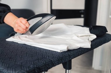 Woman using steaming iron to ironing fashion shirt in laundry room. Girl doing stream vapor iron for press clothes in hand.