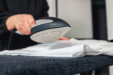 Woman using steaming iron to ironing fashion shirt in laundry room. Girl doing stream vapor iron for press clothes in hand.