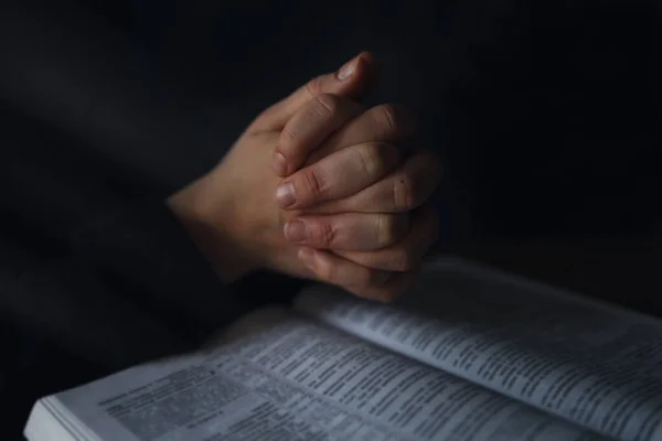 Woman hands on Bible. she is reading and praying over bible in a dark space over wooden table.