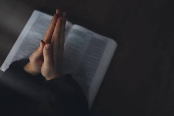 女性は 聖書を手します 読み取りおよび木製のテーブルの上暗い空間では 聖書を祈る — ストック写真