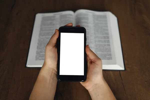 Woman hand hold and touch screen smart phone,cellphone in church over blurred bible holy and age book.