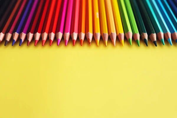 Line of colored pencils on yellow background top view. Rainbow palette wood pencils. School supplies for kids.