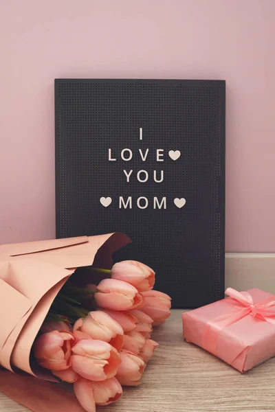 Beautiful tulips with the letter I LOVE MOM on letterboard sign. Pink background, frame, border. Lovely greeting card with tulips for Mothers day, wedding or happy event concepts.
